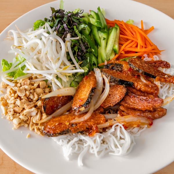 A vibrant Vietnamese noodle bowl with grilled pork, fresh vegetables, peanuts, and bean sprouts.