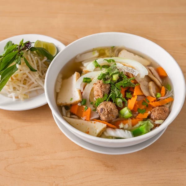 Happy Veggie's vegan pho with tofu, vegan meatballs, carrots, and onions, served with a side of basil, bean sprouts, and lime.