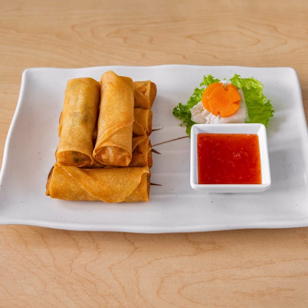 Crispy golden spring rolls on a white rectangular plate with sweet chili sauce and garnish.