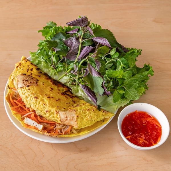 A vegan Vietnamese sizzling crepe (Banh Xeo) with fresh herbs and dipping sauce.
