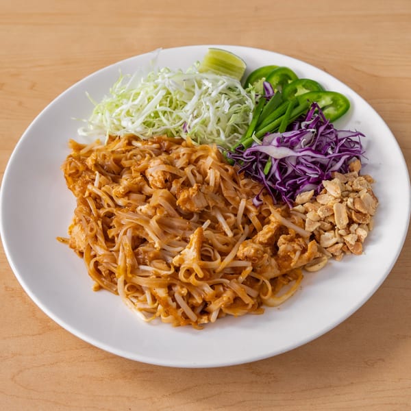 Vegan Pad Thai with noodles, tofu, bean sprouts, peanuts, shredded cabbage, and lime on a white plate.
