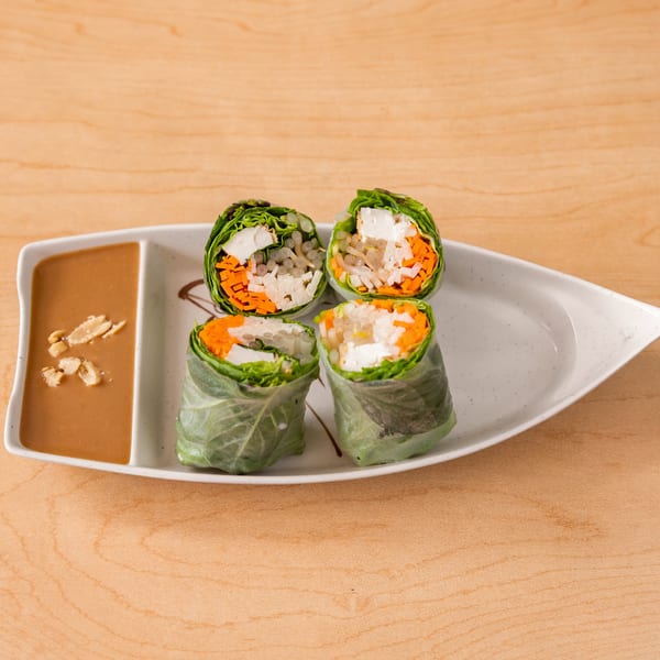 Four vegan spring rolls with tofu, carrots, and rice noodles, served with peanut sauce.
