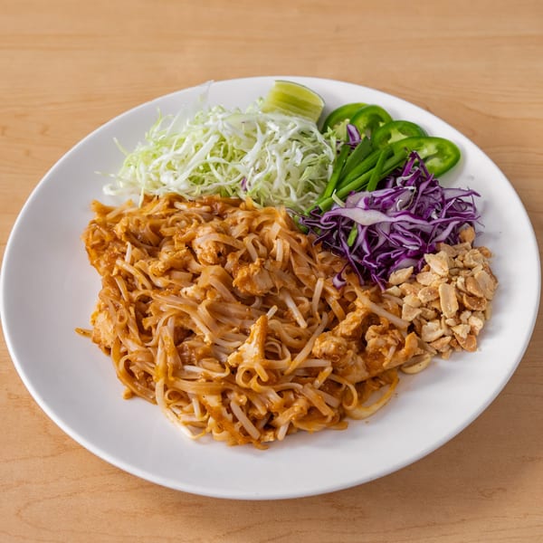Vegan Pad Thai with noodles, tofu, shredded cabbage, lime, jalapeños, and peanuts on a white plate.