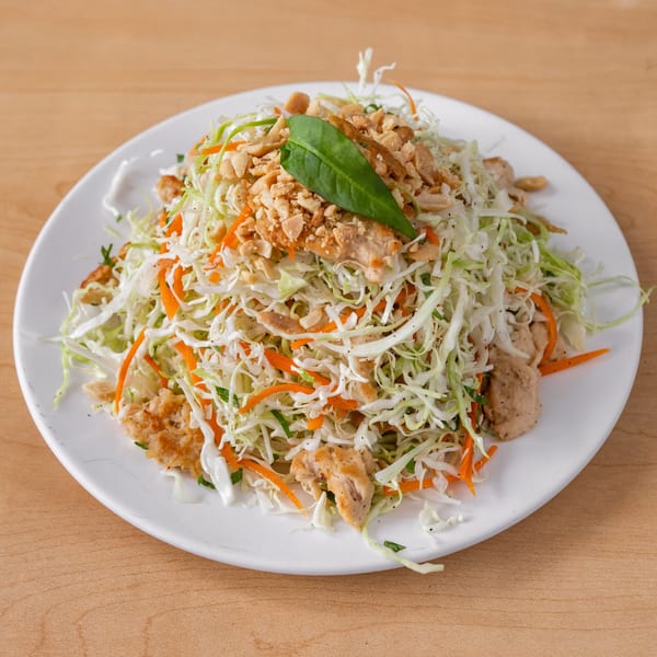 Vegan coleslaw with shredded cabbage, carrots, plant-based chicken, and crushed peanuts on a white plate.