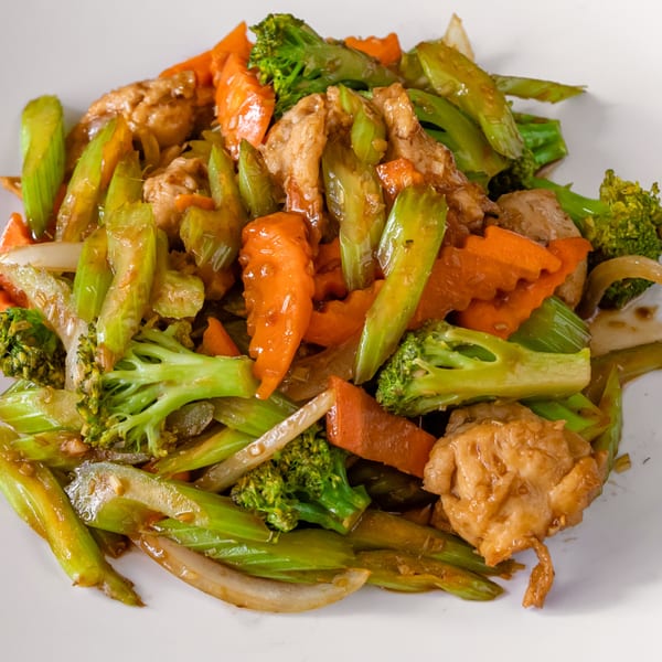 Chicken stir-fry with broccoli, carrots, and celery on a white plate.