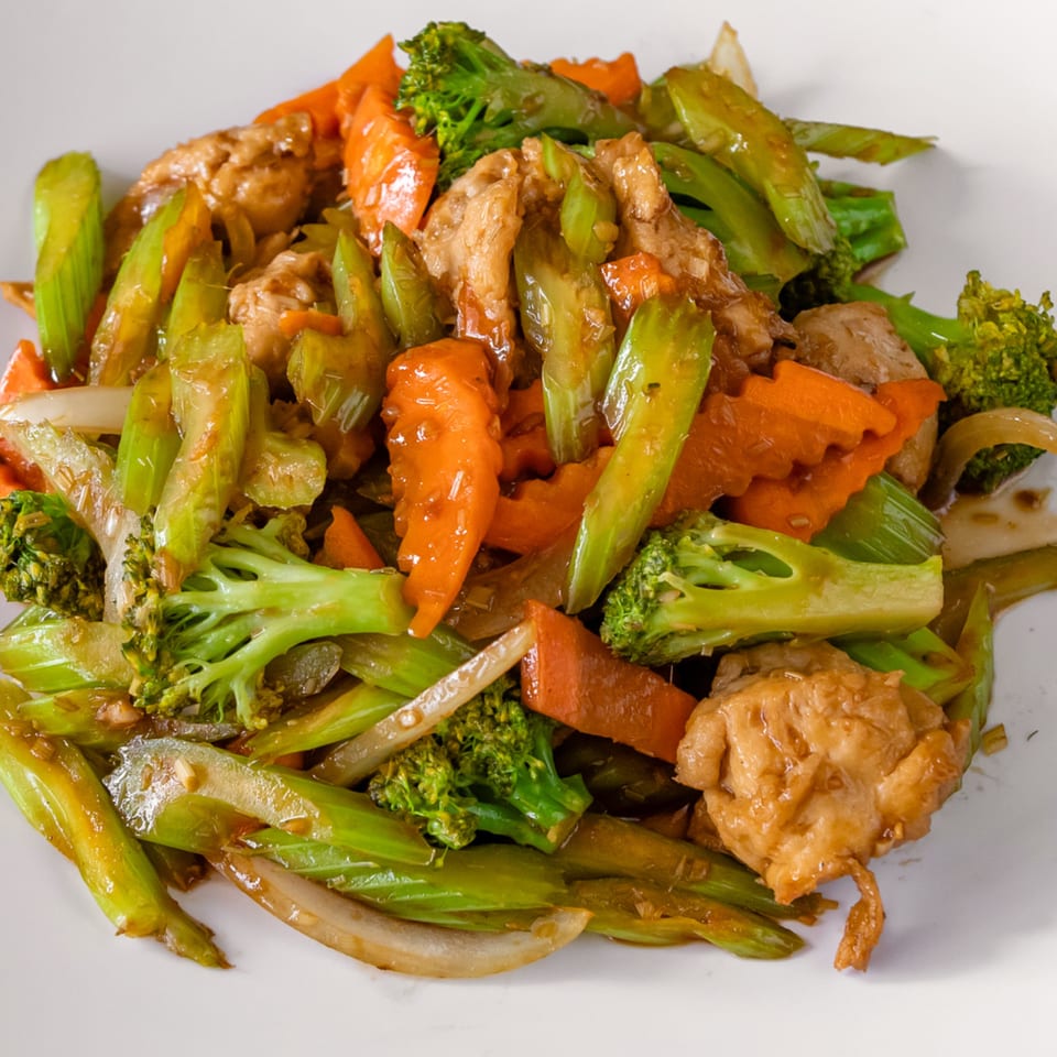 Chicken stir-fry with broccoli, carrots, and celery on a white plate.